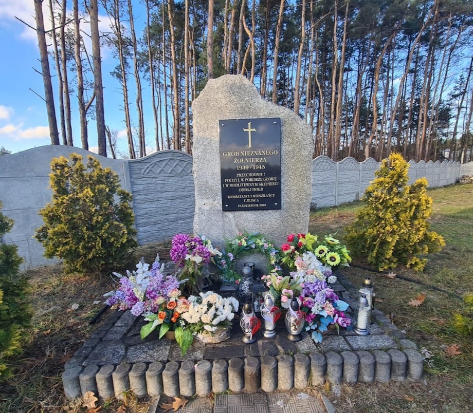 Płyta pomnika ze zniczami i kwiatami.