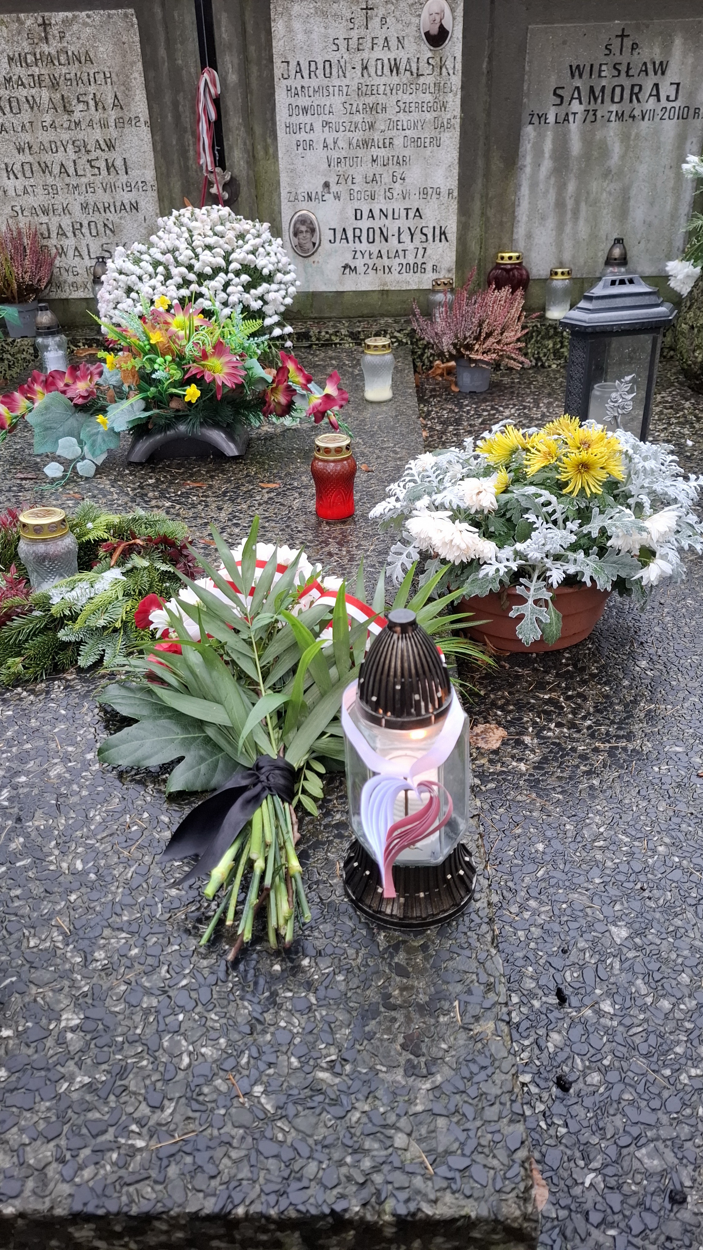 Znicz z zawieszonym papierowym biało-czerwonym sercem oraz bukiet kwiatów z biało-czerwoną wstążką