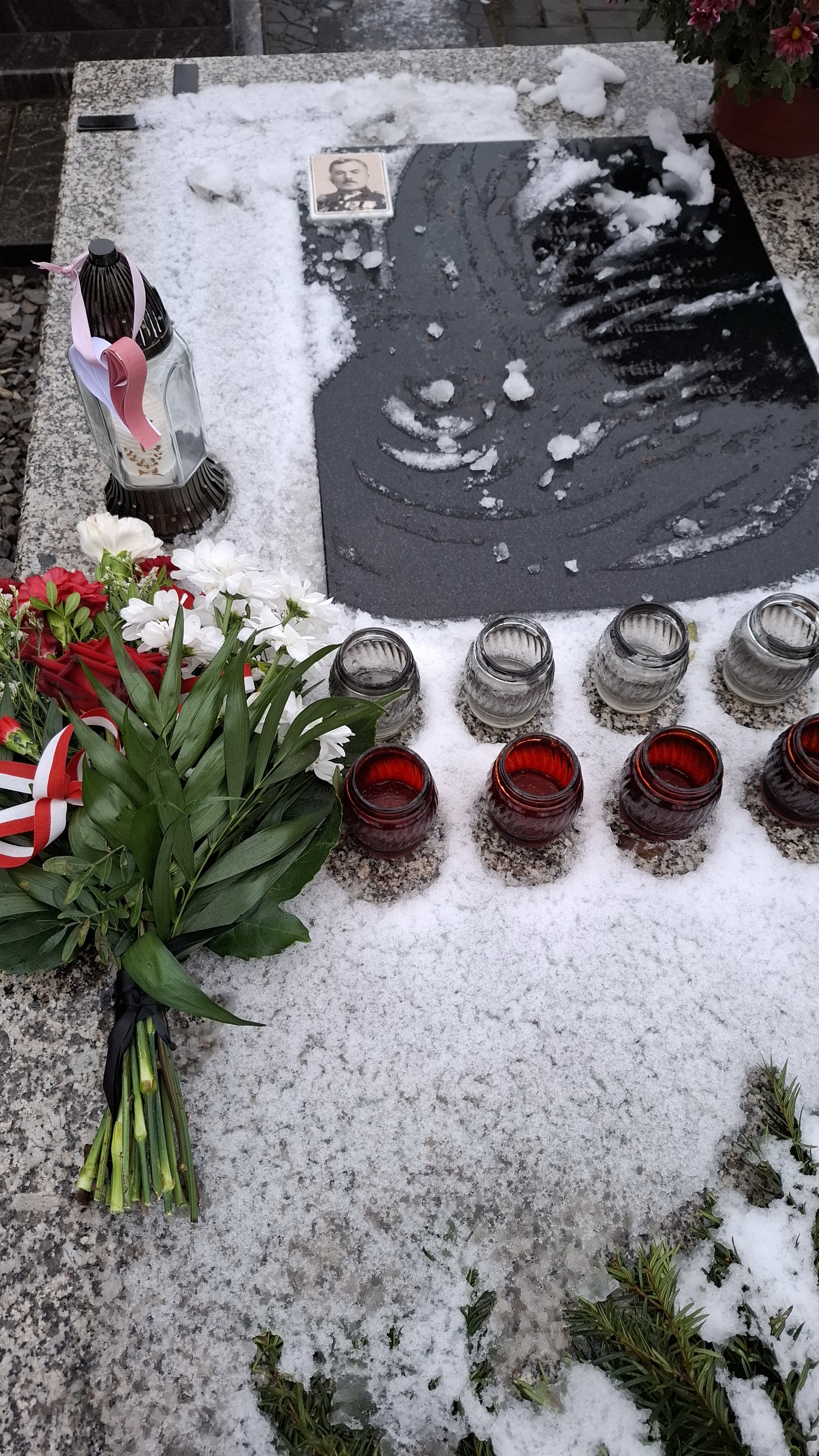Znicz z zawieszonym papierowym biało-czerwonym sercem oraz bukiet kwiatów z biało-czerwoną wstążką