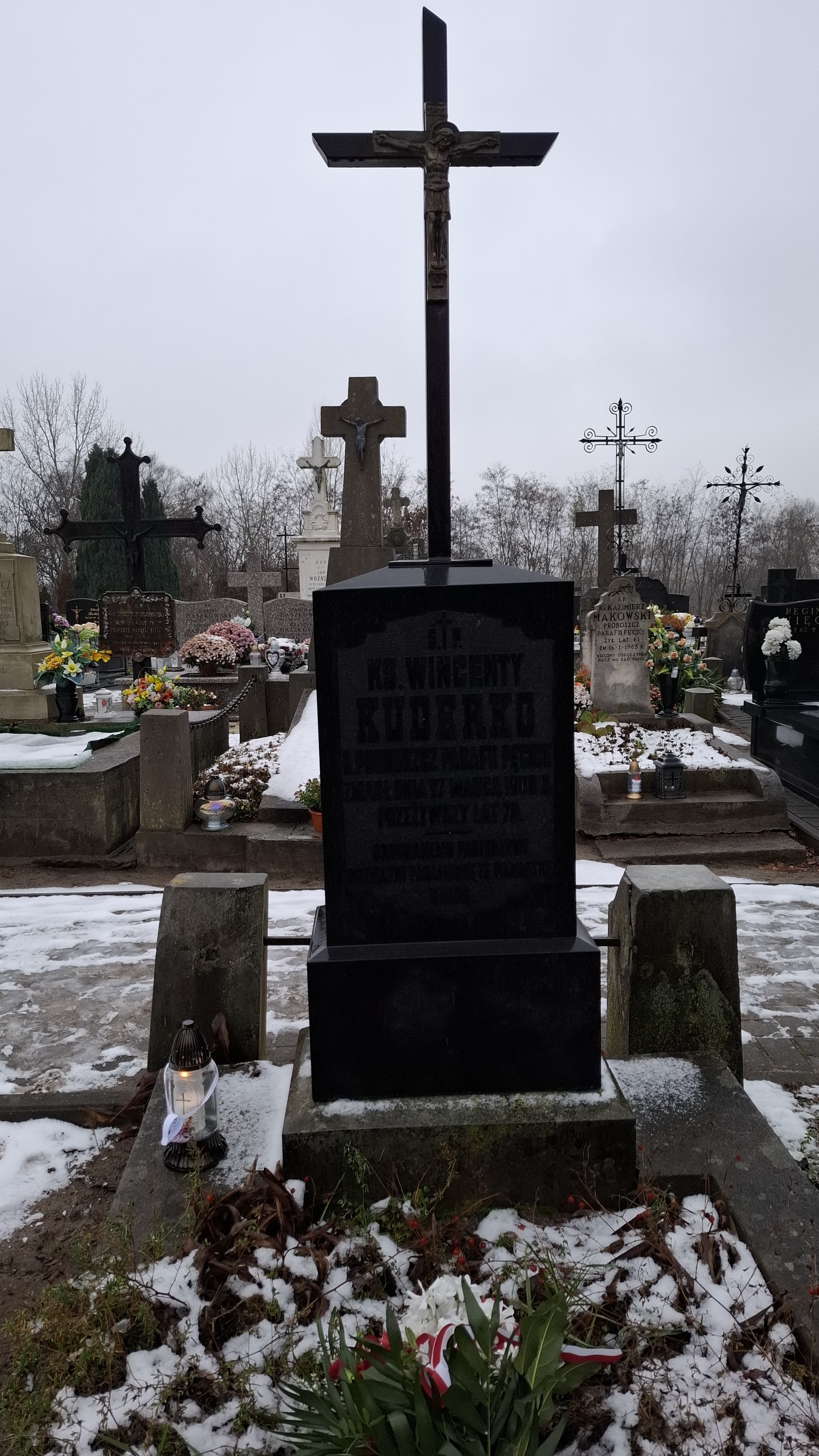 Znicz z zawieszonym papierowym biało-czerwonym sercem oraz bukiet kwiatów z biało-czerwoną wstążką