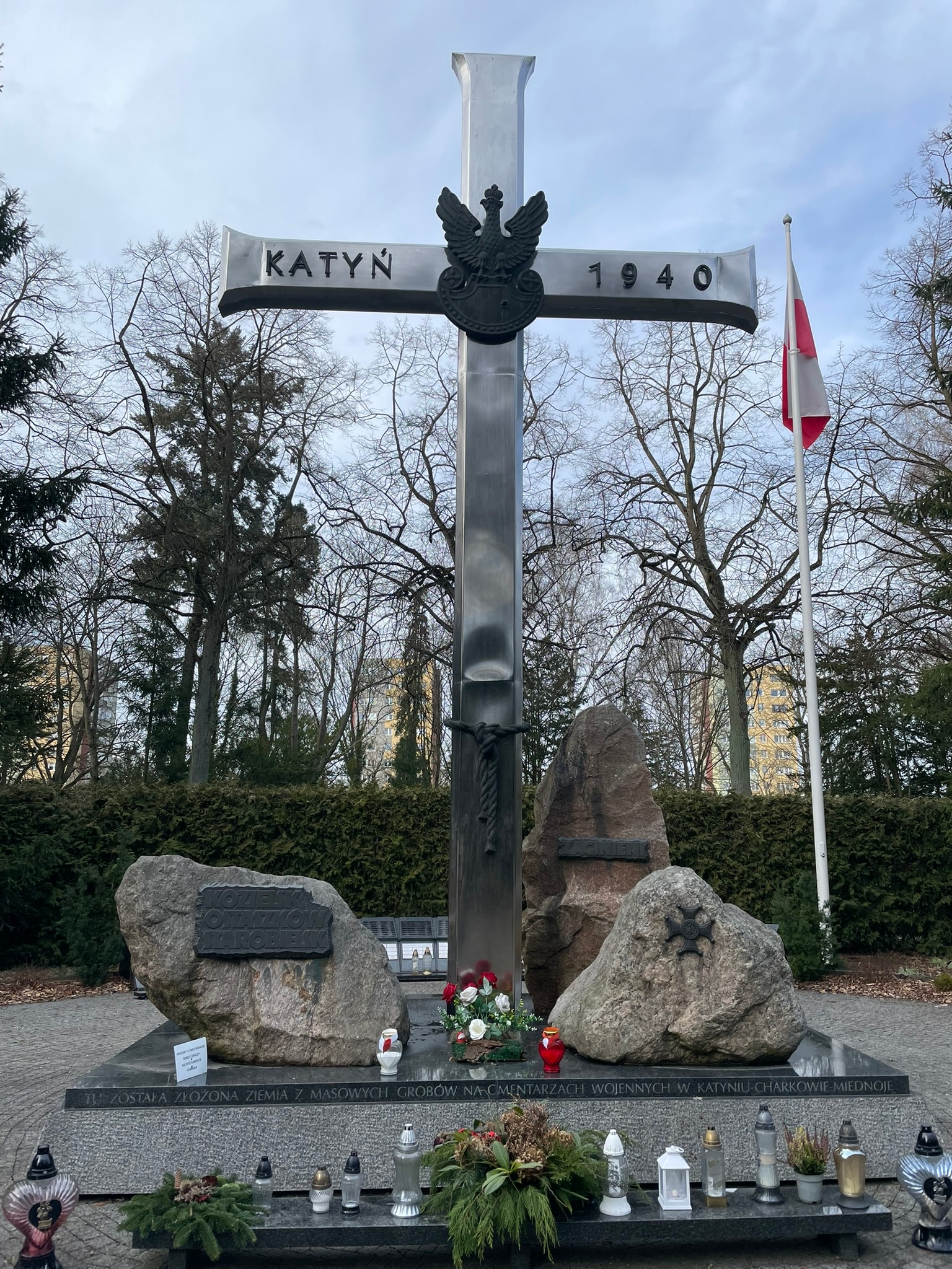 Metalowy krzyż z napisem "KATYŃ 1940". Po obu stronach trzy głazy z tablicami - nazwami obozów.