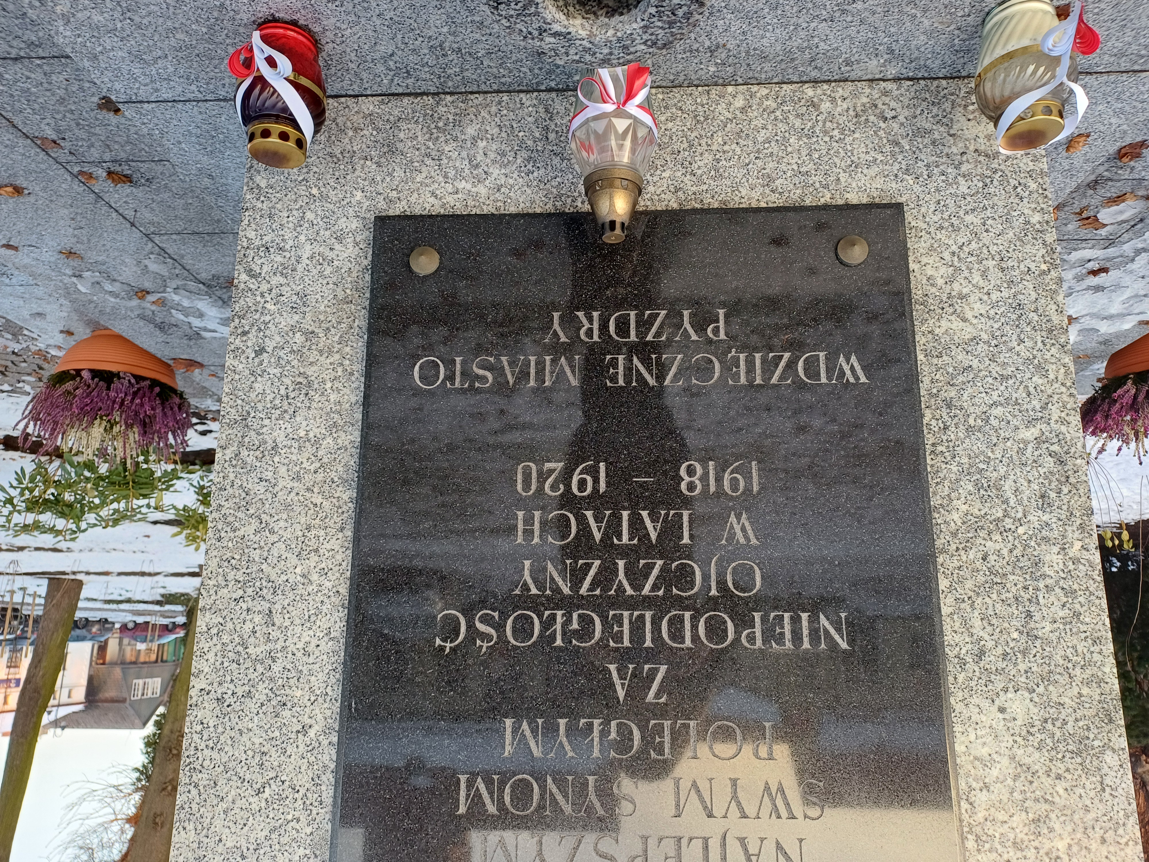 Na zdjęciu znajduje się jedna z tablic umieszczonych na pomniku i znicze z Płomieniem Pamięci.
